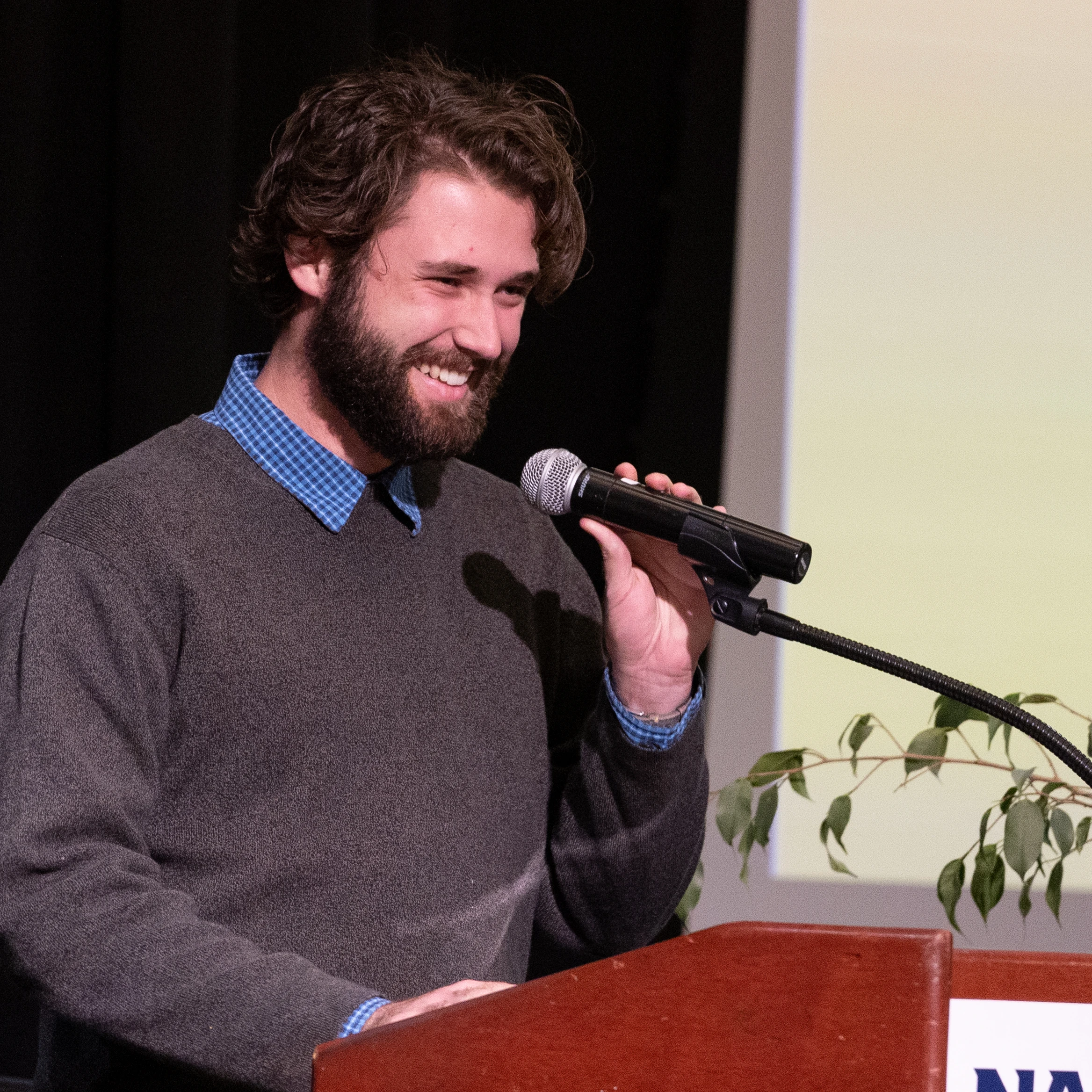 Brendan smiling as he speaks into the microphone at a podium